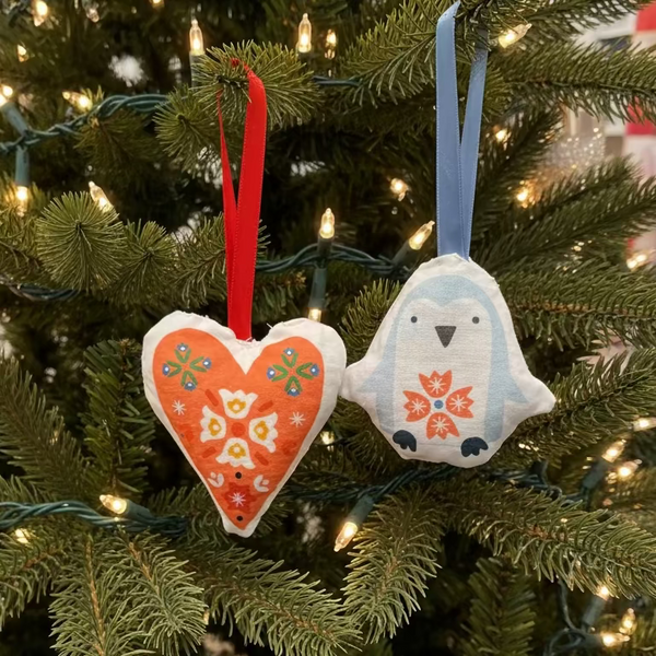 Decorative heart and penguin-shaped ornaments with floral patterns hanging in a Christmas tree.