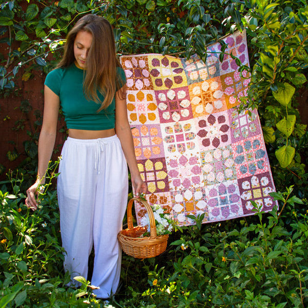Woman holding a colorful quilt in a garden setting