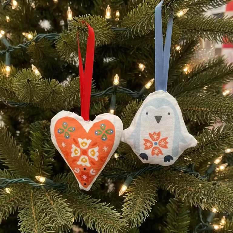 Decorative heart and penguin-shaped ornaments with floral patterns hanging in a Christmas tree.