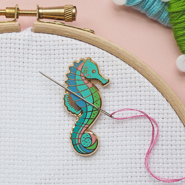 Colorful seahorse embroidery pin on fabric with a needle and thread, surrounded by yarn and an embroidery hoop.